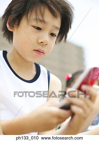 Stock Image - Young boy operating mobile phone. Fotosearch