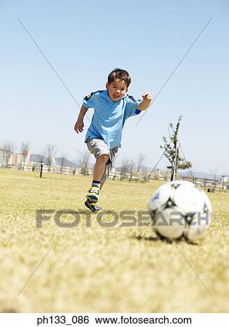 Young boy playing football on a field View Large Photo Image Stock Photograph - Young boy playing football on a field. Fotosearch