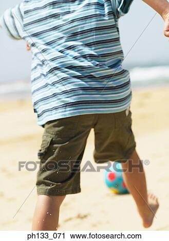 Stock Image - Young boy playing football on beach. Fotosearch