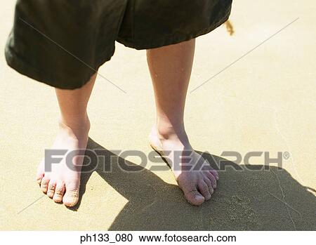 Stock Image - Young boy standing on beach barefooted. Fotosearch