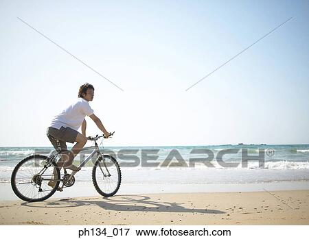 Young man cycling at beach View Large Photo Image Stock Photo - Young man cycling at beach. Fotosearch