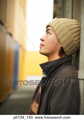 Stock Image - Young man leaning against a cargo container looking up. Fotosearch