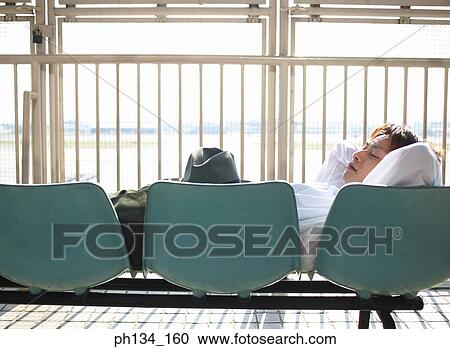 Stock Image - Young man lying on airport chairs. Fotosearch