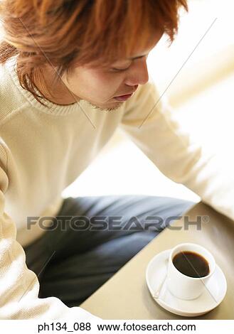 Stock Photo - Young man sitting in front of coffee cup. Fotosearch