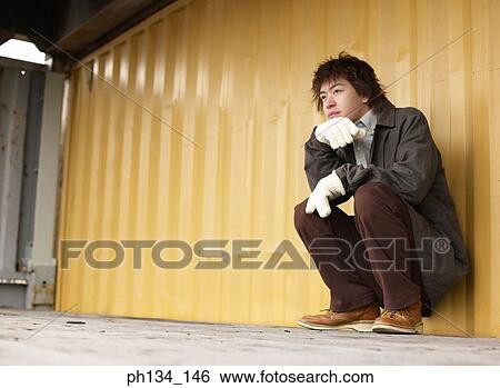 Young man sitting on floor leaning against a container View Large Photo Image Stock Photograph - Young man sitting on floor leaning against a container. Fotosearch