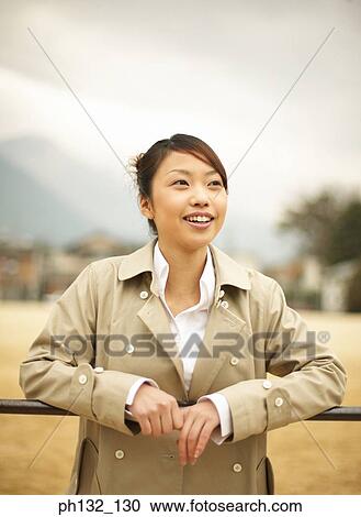 Stock Image - Young woman leaning on handrail smiling. Fotosearch