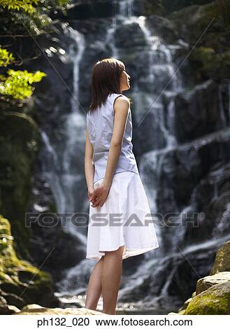 Stock Image - Young woman looking at a waterfall. Fotosearch