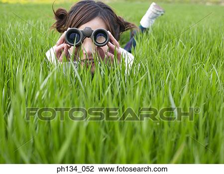 Stock Image - Young woman looking through binoculars. Fotosearch