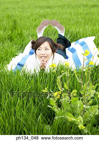 Young woman lying down in a field View Large Photo Image Stock Photo - Young woman lying down in a field. Fotosearch