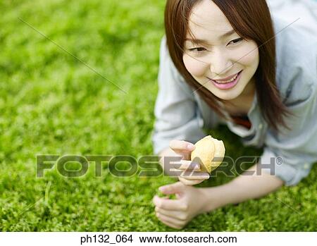 Picture - Young woman lying on ground and eating. Fotosearch