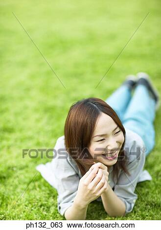 Stock Image - Young woman lying on ground and smiling. Fotosearch