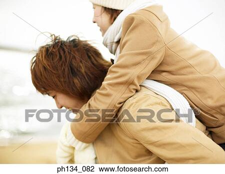 Stock Image - Young woman riding piggyback on young man. Fotosearch