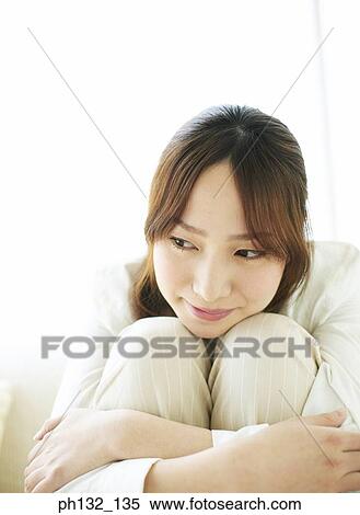 Stock Photography - Young woman sitting hugging her knees. Fotosearch