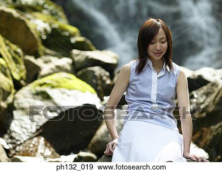 Young woman sitting in front of a waterfall View Large Photo Image Stock Photo - Young woman sitting in front of a waterfall. Fotosearch