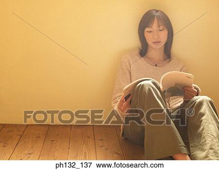 Stock Photo - Young woman sitting on floor reading a book. Fotosearch