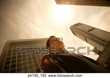 Stock Photography - Low angle view of a young businesswoman with office buildings behind. Fotosearch
