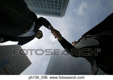 Stock Photograph - Low angle view of two young businessmen shaking hands. Fotosearch