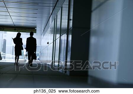 Rear view of a young businessman and a young businesswoman walking down a corridor View Large Photo Image Stock Photography - Rear view of a young businessman and a young businesswoman walking down a corridor. Fotosearch