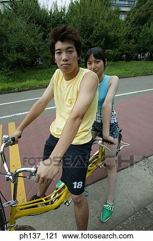 Stock Image - Teenagers riding a tandem bicycle. Fotosearch