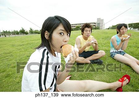 Teenagers sitting on a lawn eating hamburgers View Large Photo Image Stock Photo - Teenagers sitting on a lawn eating hamburgers. Fotosearch
