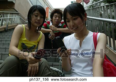 Teenagers sitting together operating their mobile phones View Large Photo Image Stock Photograph - Teenagers sitting together operating their mobile phones. Fotosearch