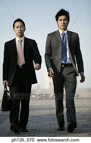 Stock Image - Two young businessmen walking outdoors. Fotosearch