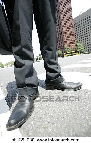 Stock Image - View of the feet of a man standing on a street crossing. Fotosearch