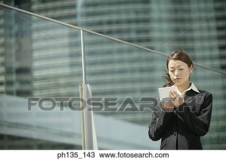 Stock Image - Young businesswoman operating a hand held device. Fotosearch
