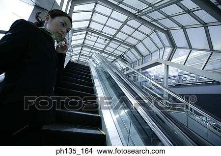 Young businesswoman standing on an escalator talking on a mobile phone View Large Photo Image Picture - Young businesswoman standing on an escalator talking on a mobile phone. Fotosearch