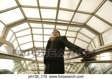 Young businesswoman standing on an escalator talking on a mobile phone View Large Photo Image Stock Image - Young businesswoman standing on an escalator talking on a mobile phone. Fotosearch