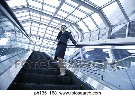Young businesswoman standing on an escalator talking on a mobile phone View Large Photo Image Stock Photo - Young businesswoman standing on an escalator talking on a mobile phone. Fotosearch
