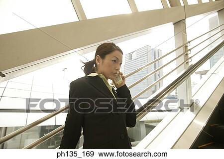 Young businesswoman standing on an escalator talking on a mobile phone View Large Photo Image Stock Photo - Young businesswoman standing on an escalator talking on a mobile phone. Fotosearch