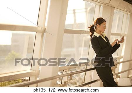 Young businesswoman standing operating a hand held device View Large Photo Image Stock Image - Young businesswoman standing operating a hand held device. Fotosearch