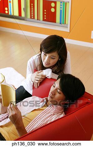 Young couple sitting on a couch reading a book View Large Photo Image Stock Image - Young couple sitting on a couch reading a book. Fotosearch