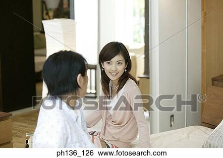 Young couple sitting together on a bed View Large Photo Image Stock Photograph - Young couple sitting together on a bed. Fotosearch