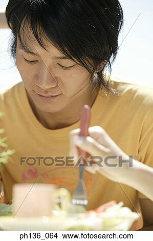 Picture - Young man seated at a table looking down. Fotosearch