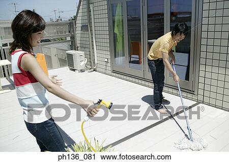Stock Image - Young woman holding a hose and a man using a mop. Fotosearch