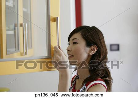 Stock Photography - Young woman opening a kitchen cabinet door. Fotosearch
