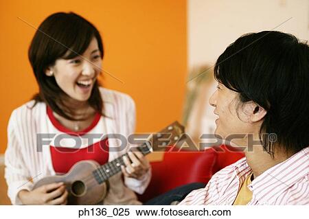 Stock Photography - Young woman playing a guitar and a man looking at her. Fotosearch