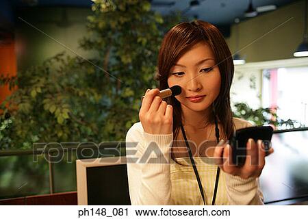Stock Image - Close-up of a businesswoman applying blush on her face. Fotosearch