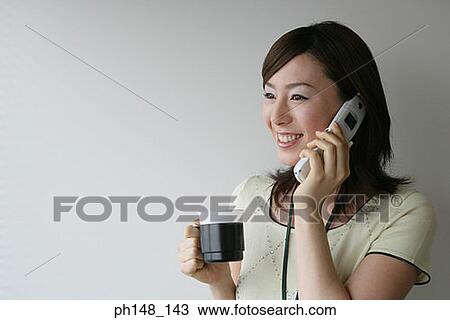 Stock Image - Close-up of a businesswoman holding a mug while using a mobile phone and smiling. Fotosearch