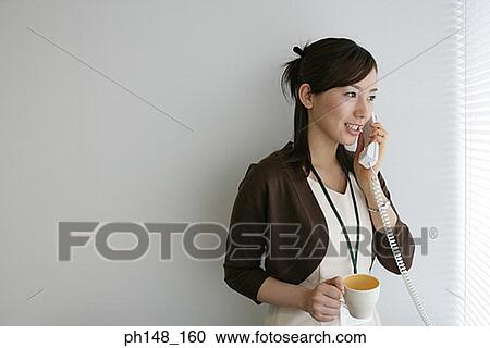 Stock Image - Close-up of a businesswoman holding a mug while talking on the telephone and smiling. Fotosearch