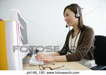 Stock Image - Close-up of a businesswoman wearing headset and using a computer. Fotosearch