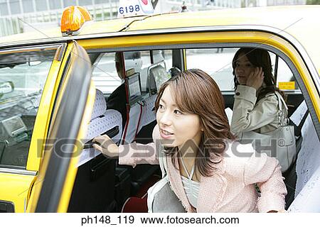 Stock Photo - Close-up of a young woman and her friend using a mobile phone in a car. Fotosearch
