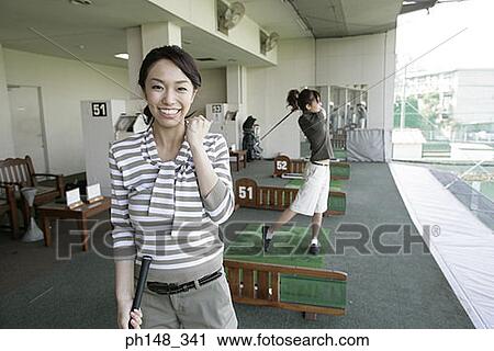Stock Image - Close-up of a young woman playing golf with another young woman in the background. Fotosearch