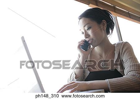 Close-up of a young woman talking on a mobile phone and using a laptop View Large Photo Image Stock Image - Close-up of a young woman talking on a mobile phone and using a laptop. Fotosearch