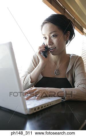 Close-up of a young woman talking on a mobile phone and using a laptop View Large Photo Image Stock Image - Close-up of a young woman talking on a mobile phone and using a laptop. Fotosearch
