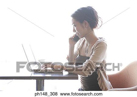 Close-up of a young woman talking on a mobile phone and using a laptop View Large Photo Image Stock Photo - Close-up of a young woman talking on a mobile phone and using a laptop. Fotosearch