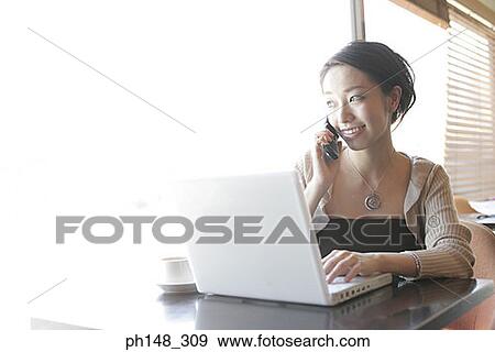 Close-up of a young woman talking on a mobile phone and using a laptop View Large Photo Image Stock Photo - Close-up of a young woman talking on a mobile phone and using a laptop. Fotosearch