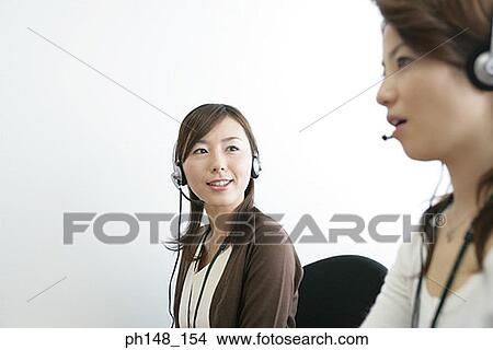 Close-up of two businesswomen wearing headset in an office and smiling View Large Photo Image Picture - Close-up of two businesswomen wearing headset in an office and smiling. Fotosearch
